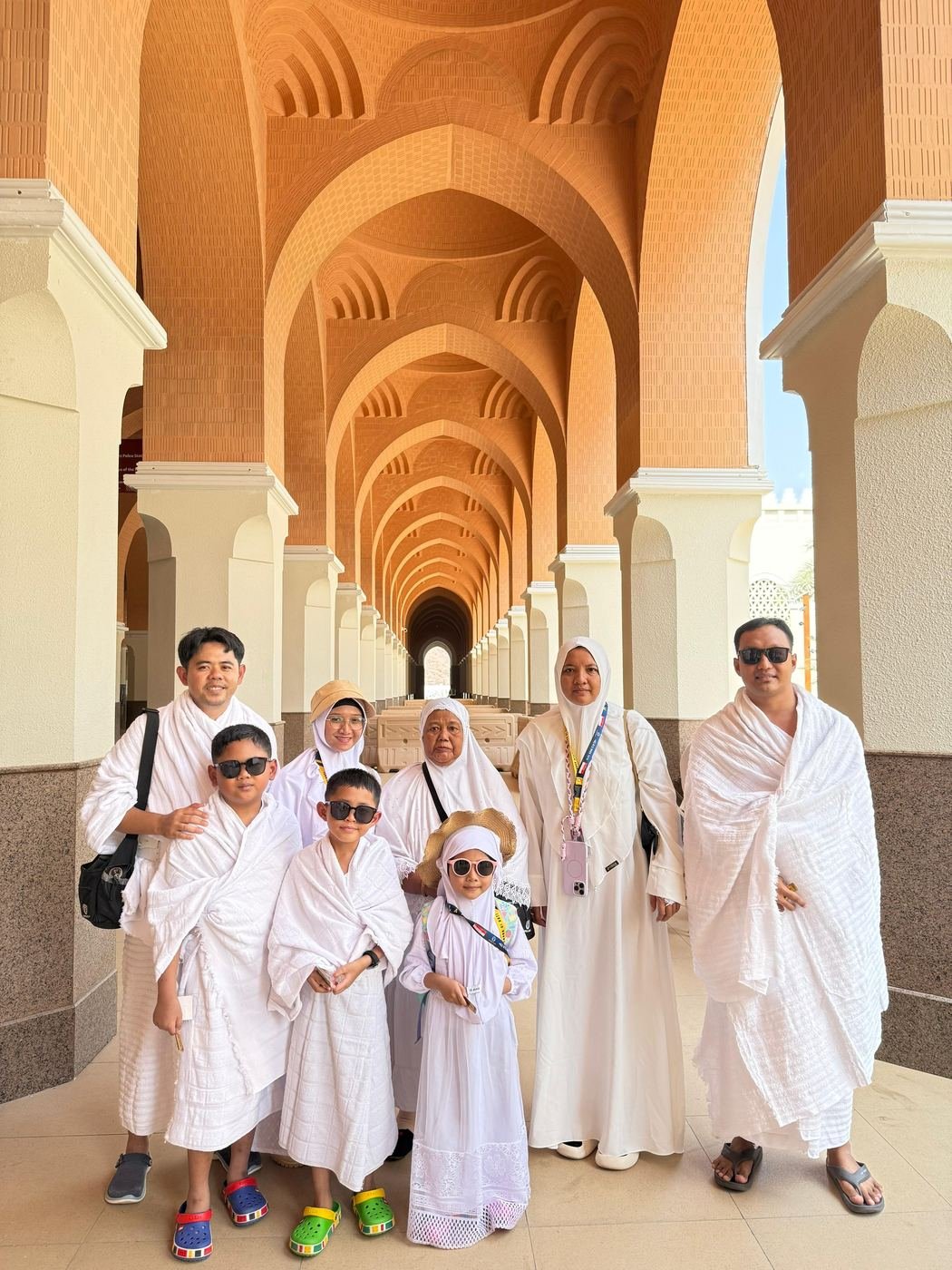 Keluarga jamaah Husnul Islam, termasuk anak-anak, berpakaian ihram di lorong berarsitektur lengkung